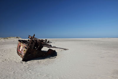 Damaged boat on beach against clear sky