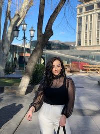 Portrait of young woman standing against building