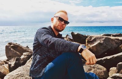 Portrait of man in sunglasses sitting on rock at beach