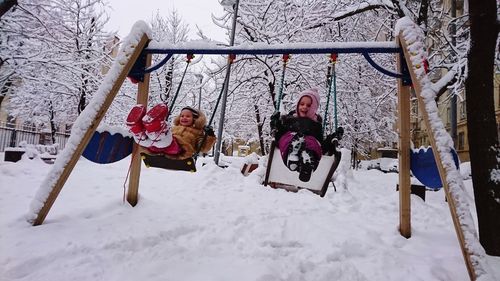Kids on swing over snow covered field during winter