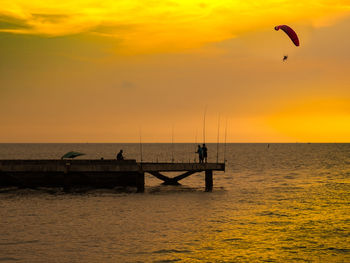 Silhouette people standing on sea against sky during sunset