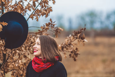 Smiling woman wearing warm clothing standing by dry plant