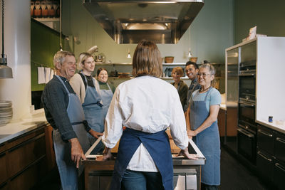 Rear view of female chef briefing multiracial students standing in kitchen
