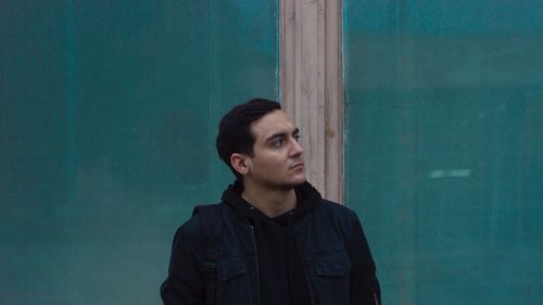 Portrait of young man looking away against blue wall