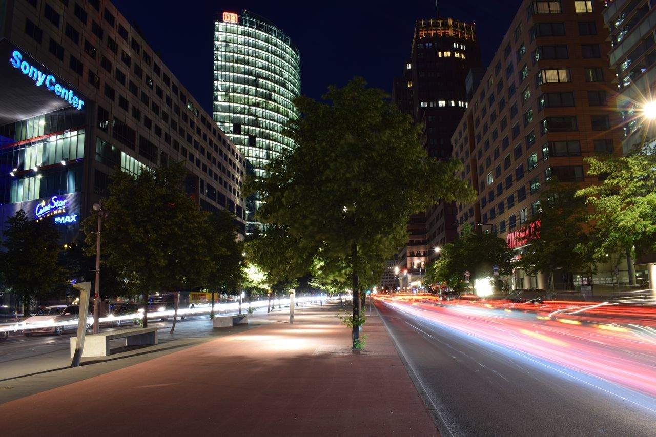 LIGHT TRAILS ON CITY STREET AMIDST BUILDINGS AT NIGHT