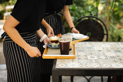 Waitress with apron serving iced coffee to customer at cafe.