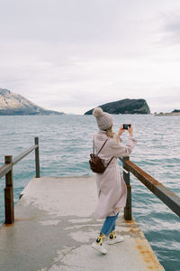 Rear view of woman standing by sea against sky