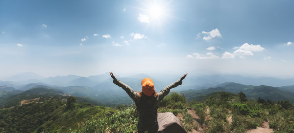 Rear view of woman with arms raised standing against mountain