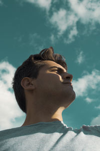 Low angle view of young man looking away while standing against sky