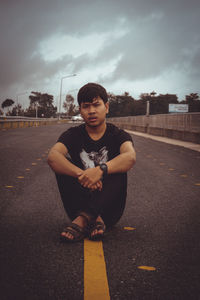 Man sitting on road in city against sky