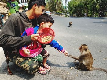 Father and son feeding monkey while crouching on road