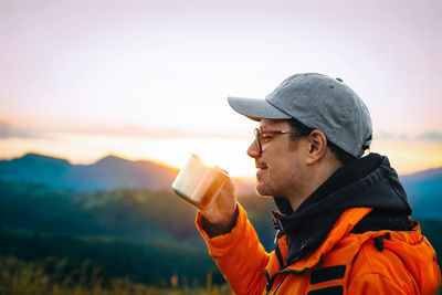 Side view of man drinking water against sky