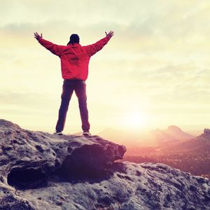 The figure of the men in red outdoor jacket on sharp cliff. mountains within early fall daybreak