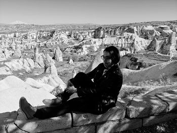 Young woman sitting on rock against sky