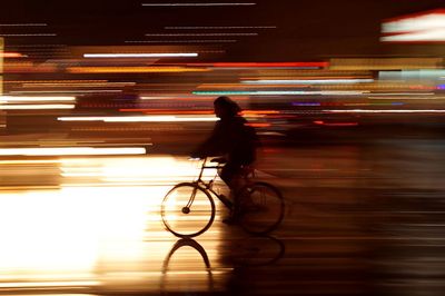 Rear view of man riding bicycle at night