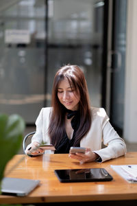 Businesswoman holding credit card and smart phone doing online shopping at desk in office