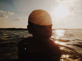 Close-up of shirtless boy in sea against sunset sky