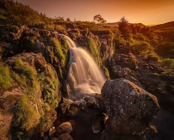 Scenic view of waterfall against sky during sunset