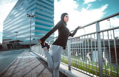 Side view of woman on railing against sky in city