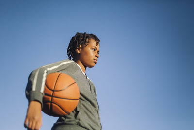 Girl looking away with basketball by clear sky