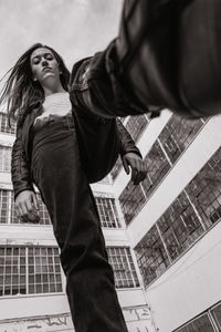 Low angle portrait of young woman walking against building in city