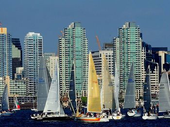 Sailboats in sea against modern buildings in city