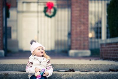 Smiling baby girl in warm clothing looking away while sitting on steps