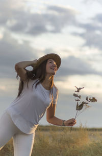 Charming model holding white flowers and posing joyful on background of rural field.