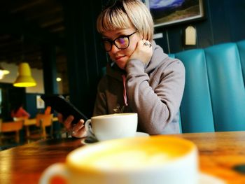 Woman using phone by coffee cup in cafe