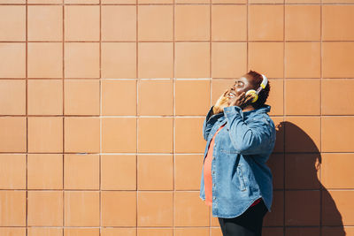 Happy woman enjoying music through wireless headphones in front of wall