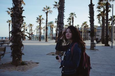 Portrait of young woman standing by palm trees