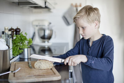 Boy slicing loaf of bread at kitchen counter