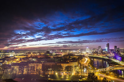 Illuminated city by river against sky at night