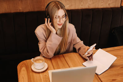 A millennial business woman with glasses works and studies online using a mobile phone in a cafe