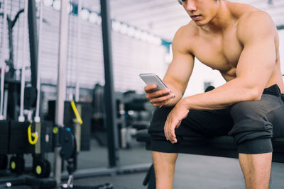 Midsection of shirtless muscular man using mobile phone in gym