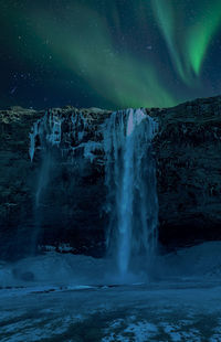 Scenic view of waterfall against aurora borealis in sky during winter