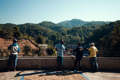 Rear view of people looking at mountains against clear sky