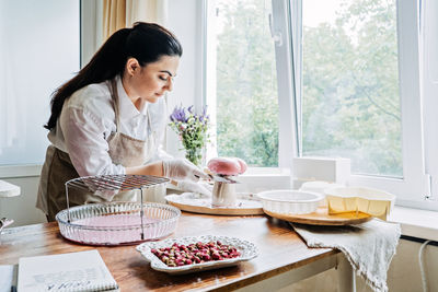 Female baker make perfect custom pink heart shape cake in kitchen bakery. online cake store. custom