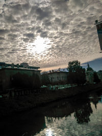 Buildings by river against sky during sunset