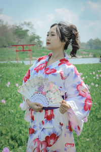 Woman wearing kimono holding hand fan while standing in park