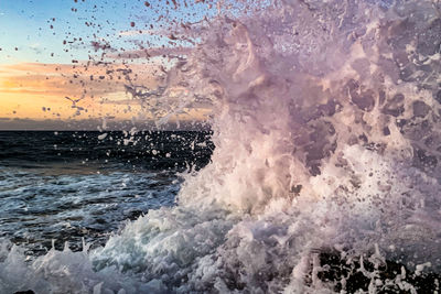 Waves splashing on rocks at shore against sky