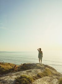 Rear view of woman standing on rock by sea against sky