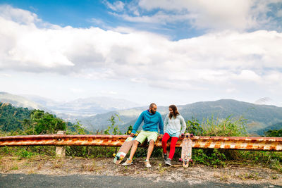 Couple sitting on railing against sky