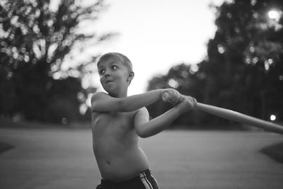 Shirtless boy swinging baseball bat on footpath