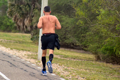 Rear view of shirtless man running on road