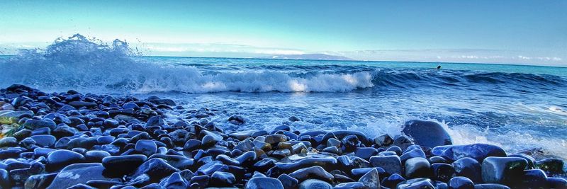 Waves splashing on rocks at shore against sky