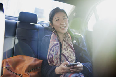 Young asian businesswoman looking at smartphone sitting in car service limousine