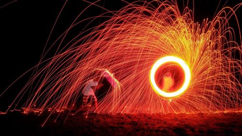 People with illuminated wire wool spinning on field at night