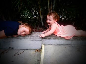 High angle view of playful sisters lying by plants at park