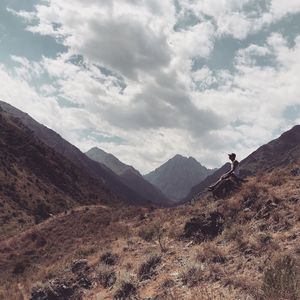 Male hiker sitting on mountain against cloudy sky